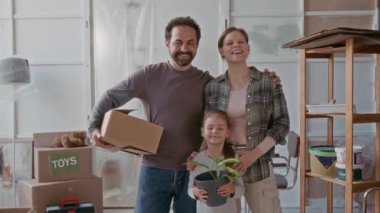 Genç çağdaş aile, baba, anne ve onların sevimli küçük kızı çiçek saksısında yeşil çiçeklerle birlikte geniş oturma odasında apartman yenileme sırasında ayakta duruyorlar.