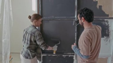 Ressamla gülümseyen genç bir kadının kocasına bakması ve yeni ev yenileme fikirleri tartışılırken oturma odasının duvarına gri boya sürmesi.