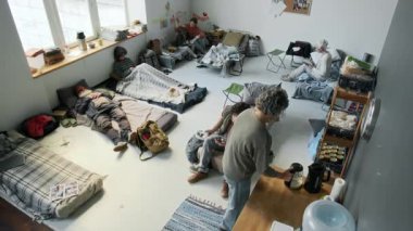 Doğal afet, sel ya da yangın nedeniyle yerlerinden edilen insanların acil durum barınağında dinlenirken, çay içerken, müzik dinlerken, anne oğluna kitap okurken geniş açılı güvenlik kamerası görüntüleri.
