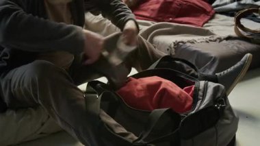 Mülteci sığınağındaki şiltede oturan, giysileri karıştıran, eşyaları arayan, kalın gri sakallı yaşlı beyaz adamın orta boy ellerini ve yüzünü çekerek.
