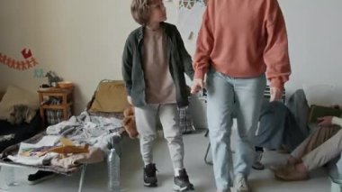 Mülteci anne ve beyaz çocuğun orta boy görüntüsü, oyuncak ayıyı tutarken, acil durum sığınağında yürürken, el ele tutuşurken, konuşurken, diğer kurtulanlar sohbet ederken ve çay yaparken.