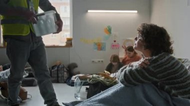 Orta ölçekli, sarı yelek giyen, depresyondaki kadına su veren, doğal afet ya da savaşla yerlerinden edilen, sığınakta şiltede oturan ve kendisine teşekkür eden bir erkek gönüllü.