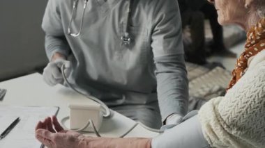 Mülteci kampındaki yaşlı beyaz kadın için kan basıncını ölçerken yüz maskesi, sphygmomanometre pompalayan eldiven ve sağlık görevlisi erkek hemşirelerin orta boy yakın çekimleri.