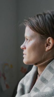 Gözü yaşlı, sıkıntılı, beyaz bir kadının dikey portresi, omuzları boş, kaçakçılık, şiddet ya da tacize uğramış, mülteci kampında poz vermiş, kameraya bakıyor.