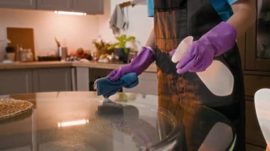 Üniformalı, tanınmayan birinin dairede bez ve deterjan kullanarak temizlik hizmeti verirken çekilmiş görüntüsü.