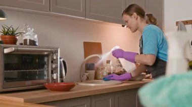 Beyaz kadın temizlikçinin, koruyucu üniformalı, lavaboya deterjan sıkarken ve temizlerken orta boy yavaş çekim.