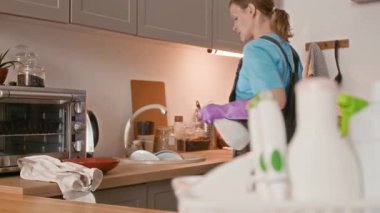 Ev ortamında lavabo ve mutfak tezgahlarını yıkarken deterjan kullanan kadın giyim ve lastik eldiven uzmanlarının dikkatlerini topla.