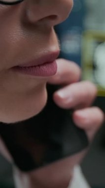 Beyaz doktor önlüklü ya da bluzlu, nötr rujlu, gözlüklü, cep telefonuyla konuşan kimliği belirsiz, kimliği belirsiz, profesyonel bir kadının dikey yakın çekimi.