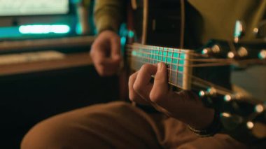 Modern neon ışıklı kayıt stüdyosunda gitar çalan tanınmayan bir sanatçının ellerinin yakın plan görüntüleri, arka planda ekran görüntüsü