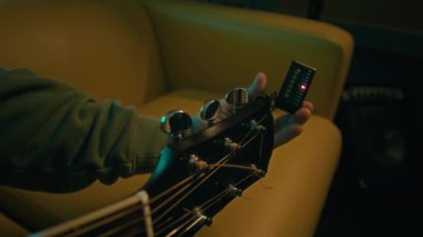 Neon ışıklı odada ayar yapmak için akustik gitar başlığının dijital elektronik akort klipsini tamir eden tanınmayan müzisyenin elleri yakın plan.