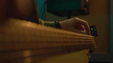 Tanınmayan gitaristin, akustik gitarın vidalarını çevirirken, loş stüdyodaki dijital elektronik akortçuyu kullanırken yakın plan çekimleri.