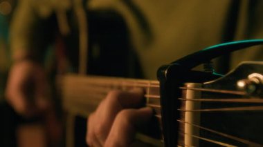 Gitar çalan ve loş bir odada Capo 'yu hareket ettiren tanınmayan müzisyenin yakın çekimi.