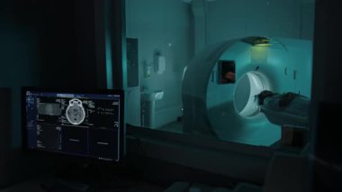 Klinikte bilgisayarın başında oturan, uzaktan kumandalı MRI makinesini çalıştıran, hastanın beyin tomografisi taraması için tarama masasına kaymasını izleyen orta ölçekli kadın radyoloji uzmanı.
