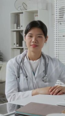 Modern veteriner kliniklerinin ofisinde çalışırken steteskopla kameraya bakan genç ve sırıtan esmer veterinerin dikey çekimi.