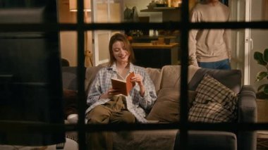 Akşamları kanepede oturan, kitap okuyan, erkek arkadaşı içeri giren, gülümseyen, sarılan ve televizyon seyretmek için yere inen beyaz bir kadının penceresinden.