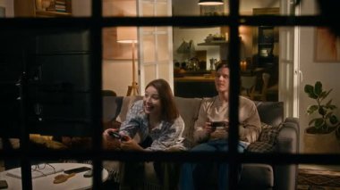 Tam kare, pencereden bakıldığında, akşamları evdeki koltukta oturan beyaz bir çift, TV 'de birlikte video oyunu oynuyorlar, kız kazanıyor, tezahürat yapıyor ve neşeyle bağırıyorlar.