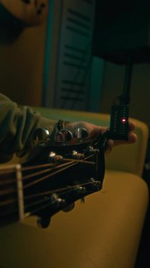 Kapalı mekanda dijital elektrikli akort cihazını kullanarak gitar başlığını ve akort aletini çeviren isimsiz müzisyenin dikey yakın çekimi