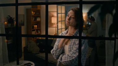 Yıldırım ve yağmur yağarken pencerenin kenarında duran, erkek arkadaşıyla tartıştıktan sonra ağlayan, arka planda volta atan beyaz bir kızın orta boy fotoğrafı.