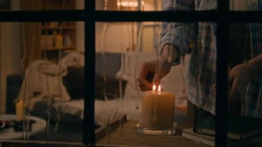 Orta boy, yabancı ya da pencereden süzülen genç beyaz kız mum yakıyor sonra kitap okumak için kanepeye oturuyor, yağmurlu havada sessiz bir gecenin tadını çıkarıyor.