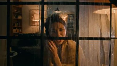 Pencereden bakıldığında, yağmurlu bir gecede pencereden dışarı bakarken omuzlarında şalla cep telefonu tartışan, çığlık atan, telefonu kapatan ve umutsuzca ağlayan genç bir kadın görülüyor.