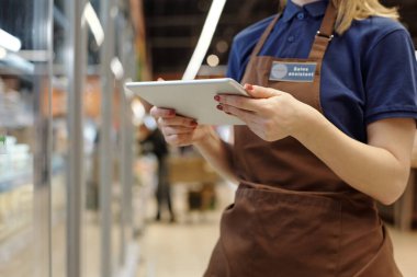 İş yerinde iş arkadaşıyla temizlik yaparken üniformalı temizlikçi ve eldivenli bez tozuyla tozları siliyor.