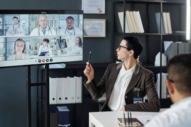 Çevrimiçi tıp konferansı sırasında ekiple konuşan insanlarla görüntülü sohbet ekranına bakan kendinden emin kadın liderin yan görünümü