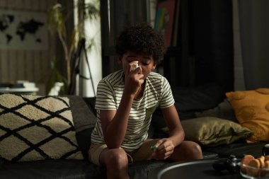 Astımı olan Afro-Amerikalı bir çocuk, kanepede otururken ağzına astım pompalayan bir astım spreyi takıyor.