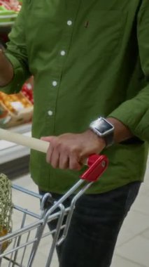 Yetişkin Hintli bir adamın markette alışveriş arabasını iterken akıllı telefon kullanmasının dikey görüntüsü.