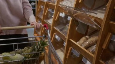 Süpermarkette fırın bölümünden geçen ve bir somun ekmeği el arabasına koyan kadın müşterilerin yakınlaştırılması, kopyalama alanı