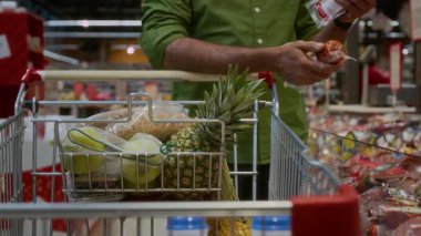 Süpermarkette et seçen ve alışveriş arabasına sosis koyan tanınmamış bir adama yakın durun.