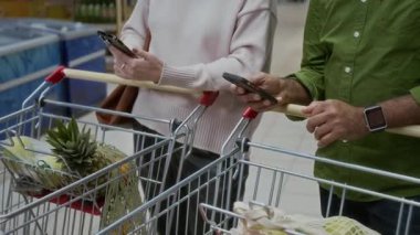 Süpermarkette telefon tutan, alışveriş listelerini ve fiyatlarını kontrol eden, fotokopi çeken iki kişi ile tanınamayan olgun çiftlerin yakınlaşması
