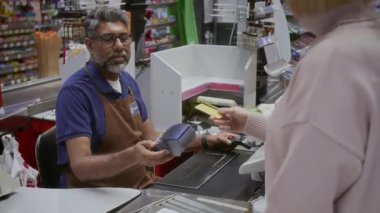 Markette kasada çalışan yetişkin Hintli bir adam ve market alışverişi yapan müşterilere bankacılık terminalini teslim etmek.