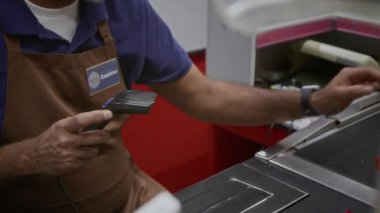 Süpermarketteki tanımlanamayan erkek veznedarın el tarayıcıya odaklanarak nesneleri taraması