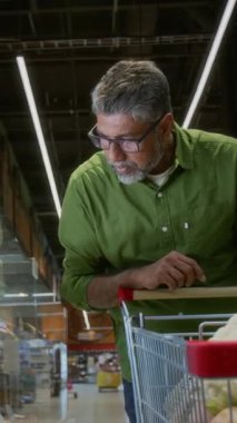 Yetişkin Hintli bir adamın markette et seçerken ve telefon kullanırken dikey görüntüsü.