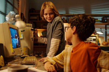 Ilık ışıkla dolu, sıcak bir odada eski moda bir bilgisayarla çevrili iki genç arkadaş, neşeli bir anı paylaşıyorlar.