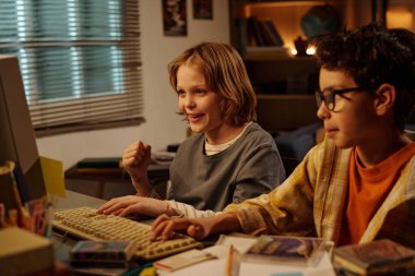 Bilgisayar ekranı ile meşgul çocuklar sıcak ve davet edici ev çalışma odasında, kitaplar ve öğrenme materyalleri ile çevrili, öğrenme hevesini gösteren