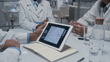 Laboratuvarda yapılan tıbbi toplantı sırasında mikroorganizmaları gösteren dijital tablet kullanan tanınmayan araştırmacıların yakın çekim görüntüleri.