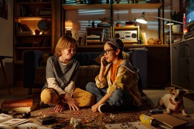 Çocuklar çeşitli oyunlar ve kitaplarla çevrili bir şekilde güzel aydınlatılmış oturma odası ortamında yerde otururken eğlenceli aktivitelere daldılar.