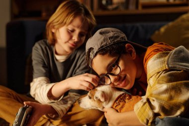 İki çocuk geceyi evde geçirir, küçük köpekle kaynaşırlar. Bir çocuk gözlük takıp köpeğini beslerken, diğer çocuk sıcak bir şekilde gülümsüyor.