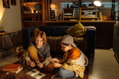 İki çocuk yerde oturuyor, köpek bakarken fotoğraf albümünün içeriğini keşfediyorlar. Kitaplarla, eski eşyalarla ve sıcak ışıklandırmayla dolu rahat bir oda davetkar bir atmosfer yaratır.