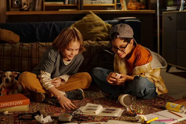 İki çocuk, rahat bir odada yerde oturmuş, rahat ifadeler takınıp, etraflarındaki teknolojiyi merak ediyorlar.