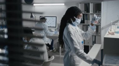 Siyahi kadın tıp araştırmacısının laboratuvarda yeni devrimci bir ilaç geliştirirken matarada çözeltiyi hazırlarken orta boy fotoğrafı.