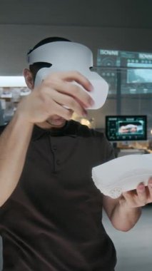 VR kulaklık takan erkek araba mühendisinin yeni sedan kil modelini taşırken orta dikey görüntüsü. Aracın dış yüzeyinde çalışırken artırılmış gerçeklik çalışma alanındaki bileşenleri manipüle ediyor.