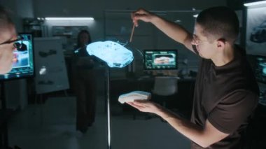 Kafkas erkek araba mühendisi ve baş tasarımcısının 3 boyutlu lazer projeksiyonunu kullanarak yeni bir geçiş modelini tartışırken, tabletli kadın meslektaşı içeri girip toplantıya katılıyor.