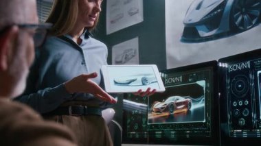 Genç beyaz kadın araba mühendisinin, dijital tablet üzerinde skeç çizerek stüdyoda üst düzey erkek takım lideriyle konuşurken orta boy fotoğrafı. Yeni sedan prototip projesini sunuyor.