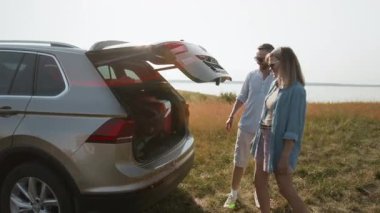 Ailelerin ve çocukların araçtan erzak indirirken ki görüntülerini büyüt, yaz haftasonu deniz manzaralı kamp gezisine hazırlanırken.