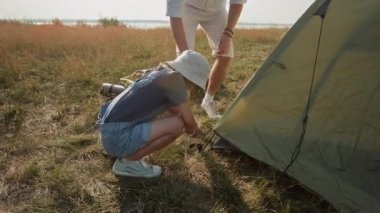 Genç neşeli kız çadır kuruyor, sonra babaya beşlik çakıyor ve göl kıyısında kamp kurarken çimenlerin üzerine düşüyor.