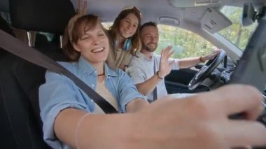 Mutlu aile yolculuğun tadını çıkarıyor, gülümsüyor ve arabada telefonla fotoğraf çekerken selfie çekiyor.