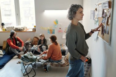 Bir grup göçmene karşı kayıp insanların fotoğraflarıyla dolu bir bildiri panosunun önünde duran olgun kadın mültecinin yan görüntüsü