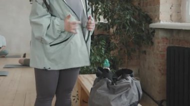 Down sendromlu genç bir kadının tavan arası yoga stüdyosuna girerken orta ölçekli bir görüntüsü. Paspas alıp nazik bayan koçla yoga yapan genç kadınlara katılıyor.